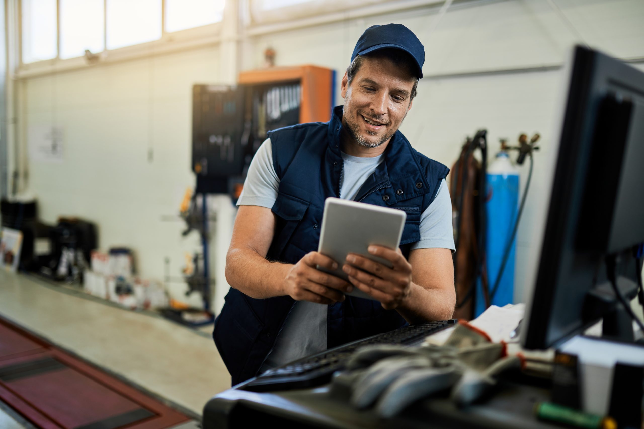 happy car mechanic using digital tablet while working auto repair shop scaled