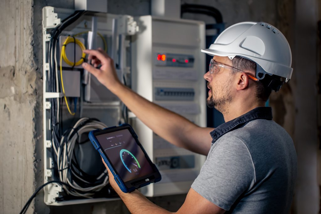 man electrical technician working switchboard with fuses uses tablet
